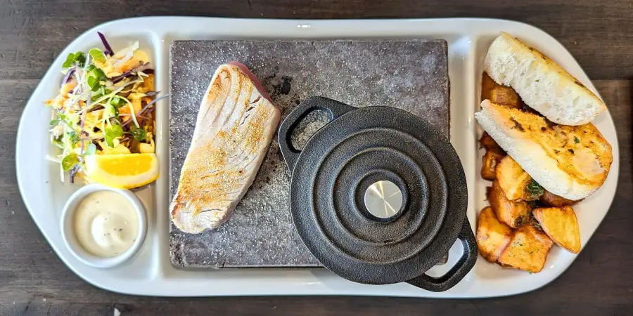 A seared tuna steak served on a hot stone with slaw, aioli and potatoes