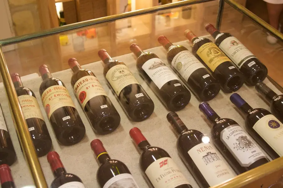 Bottles of Saint-Émilion and Pomerol laid on their sides in a locked glass retail display case, each with a small white price tag propped against it