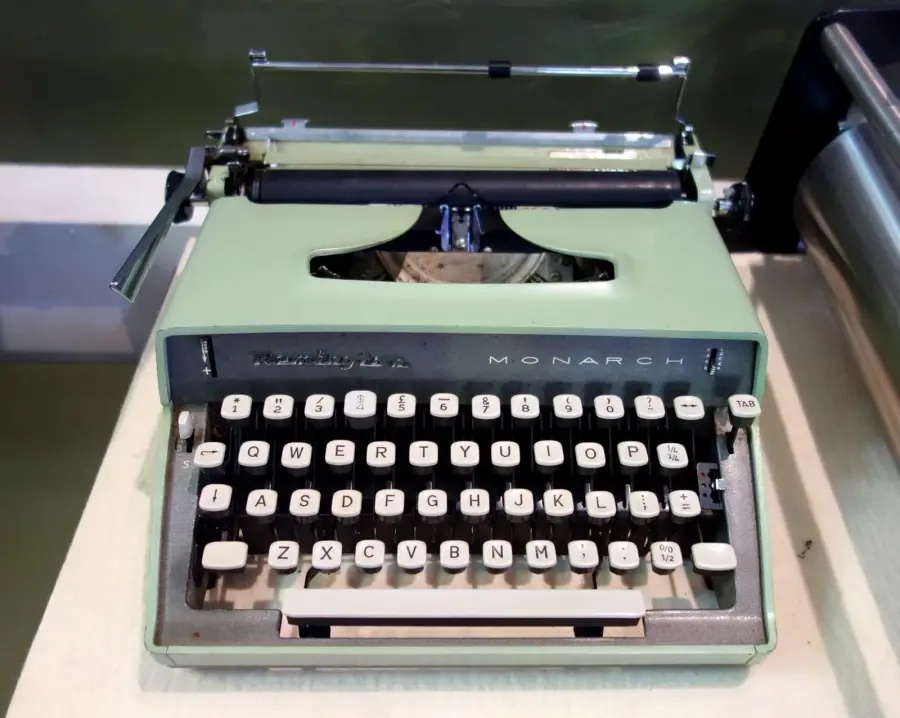 A mint green Remington Monarch portable typewriter with cream keys, displayed on a white plinth in a museum case