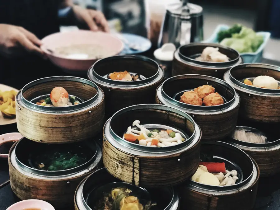 Bamboo steamer baskets of dim sum crowded on a Hong Kong breakfast table, with prawn dumplings, fish balls and mushrooms, a teapot behind