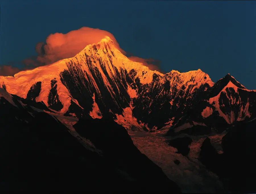 The summit of Kawagebo in the Meili Snow Mountains, Deqin, Yunnan, lit orange at sunrise above dark valleys, close to where Xige is building its Yunnan winery