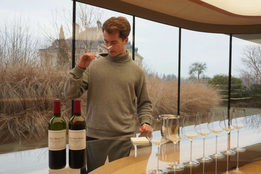 Antoine Desferet en train de sentir un verre de vin rouge au Château Haut-Bailly, bouteilles et verres de dégustation alignés