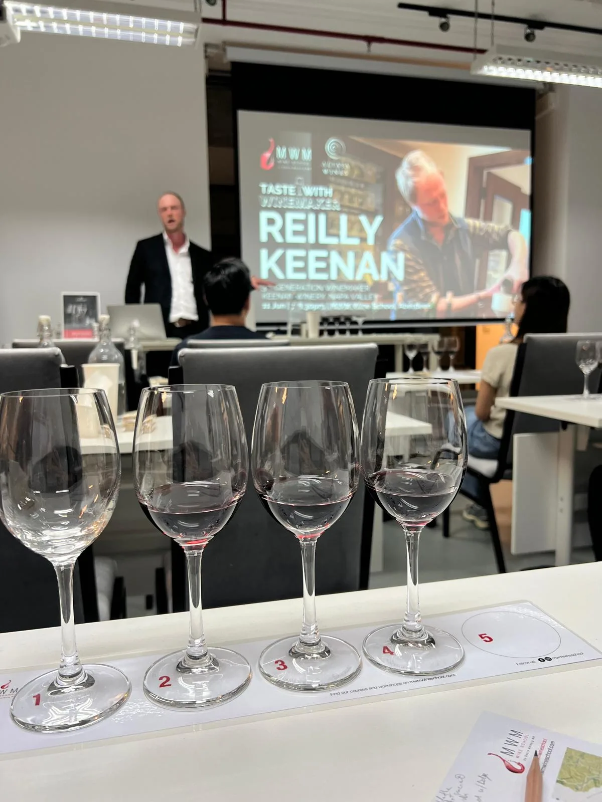 The four-wine flight, with the tasting slide behind A flight of four Keenan Winery wines in numbered glasses at the tasting in Hong Kong