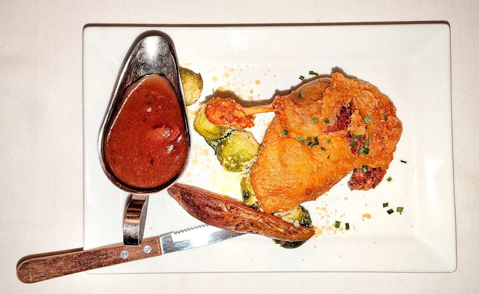 A crisp confit duck leg served with a jug of red wine sauce and Brussels sprouts