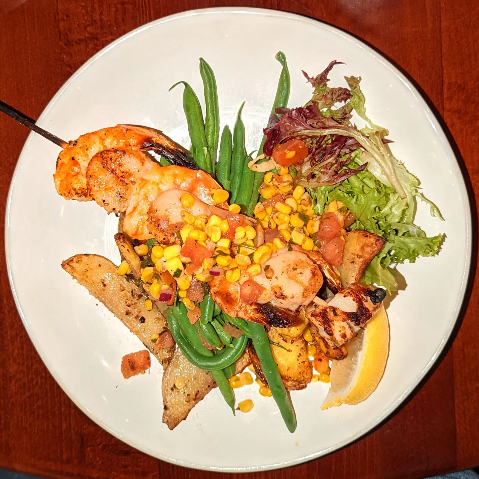 Grilled shrimp skewers served with green vegetables and a wedge of lemon