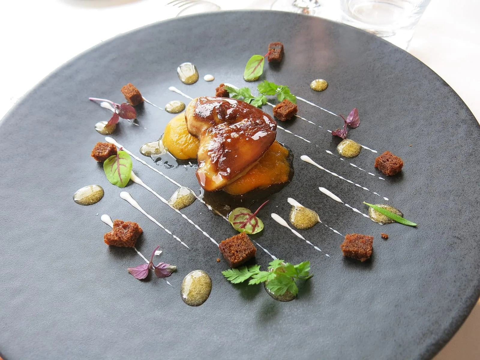 Pan-seared duck foie gras served with peach and gingerbread croutons on a slate plate