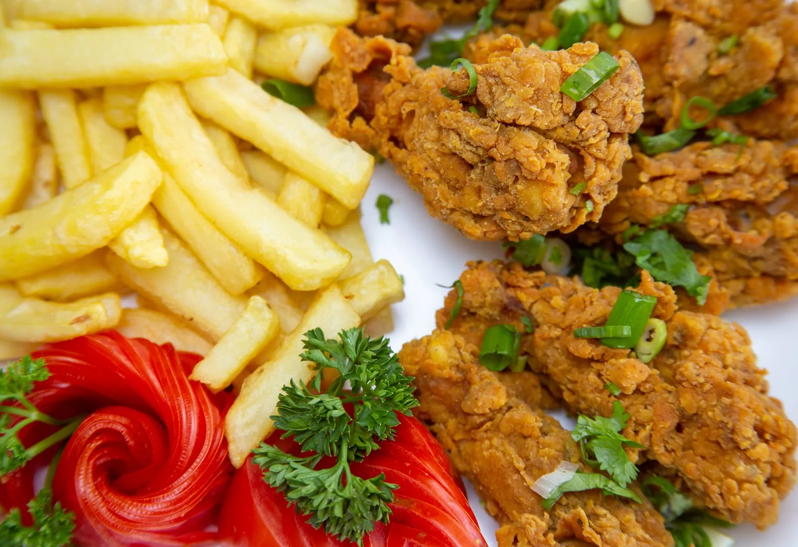 Close-up of crisp golden fried chicken pieces scattered with spring onion, served alongside a pile of chips