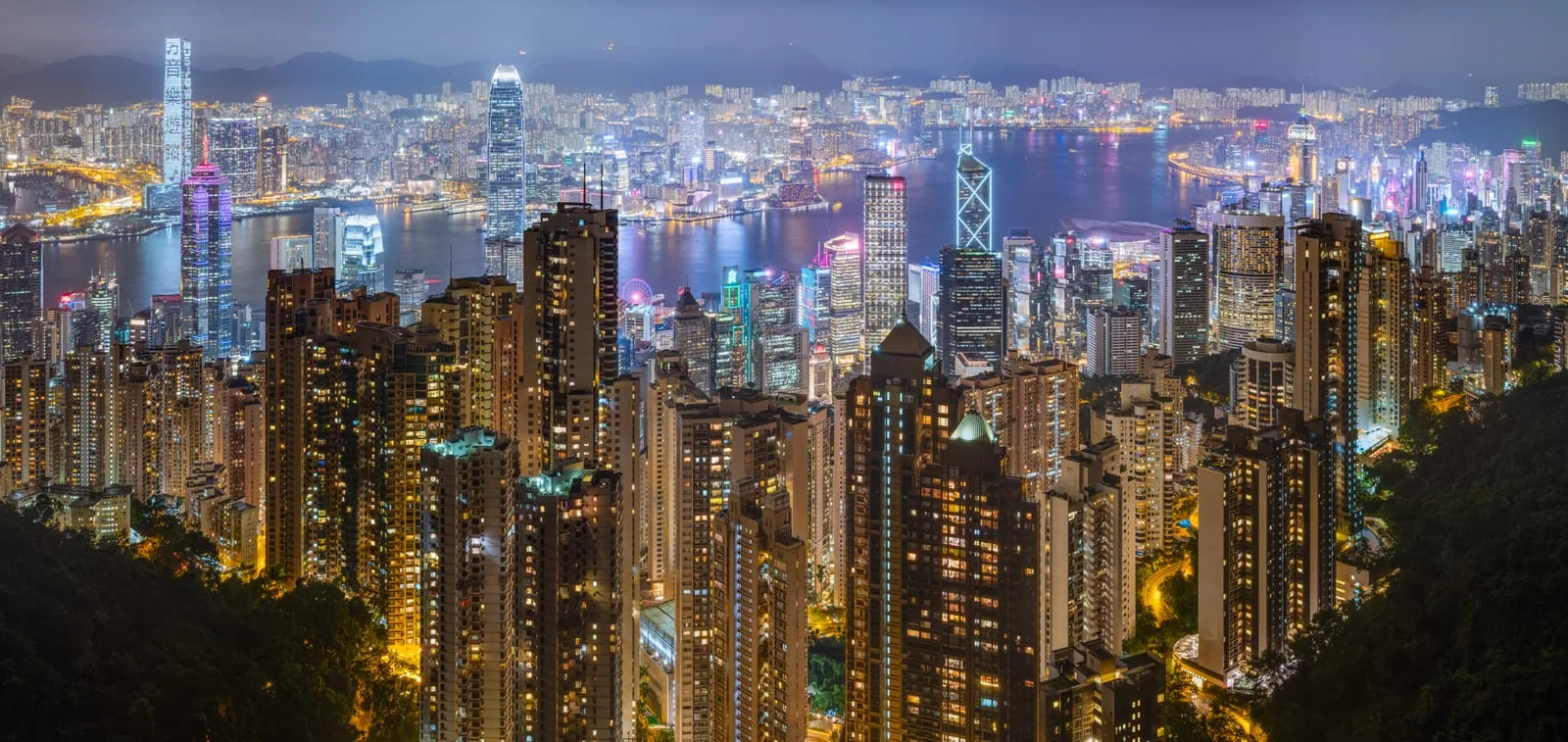Hong Kong's lit skyline and Victoria Harbour at night, seen from the Peak with towers rising on both sides of the water