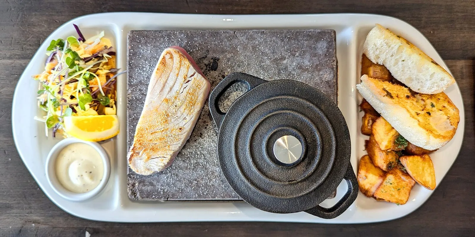 A seared tuna steak served on a hot stone with slaw, aioli and potatoes