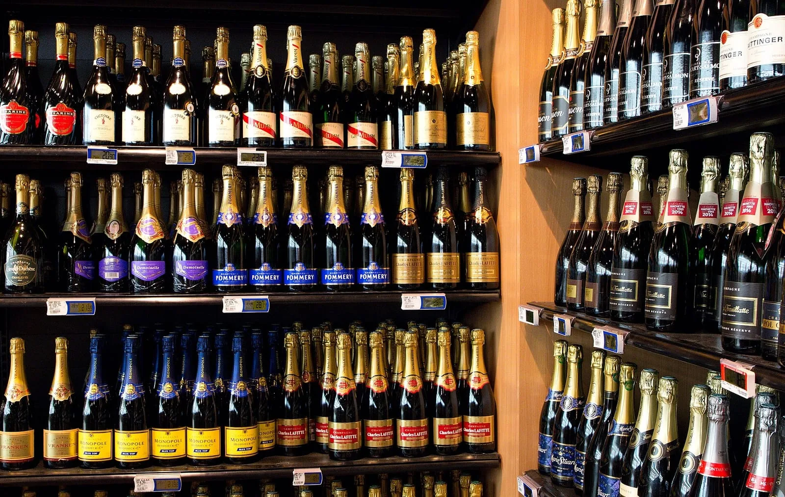 Rows of sparkling wine bottles on the shelves of a French hypermarket, with electronic price labels clipped to the rails beneath each row