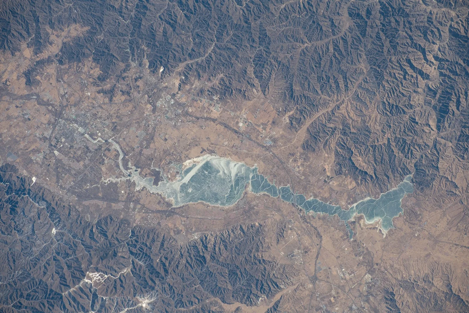 The Guanting Reservoir seen from the International Space Station, a long pale lake threading through brown mountain ridges northwest of Beijing