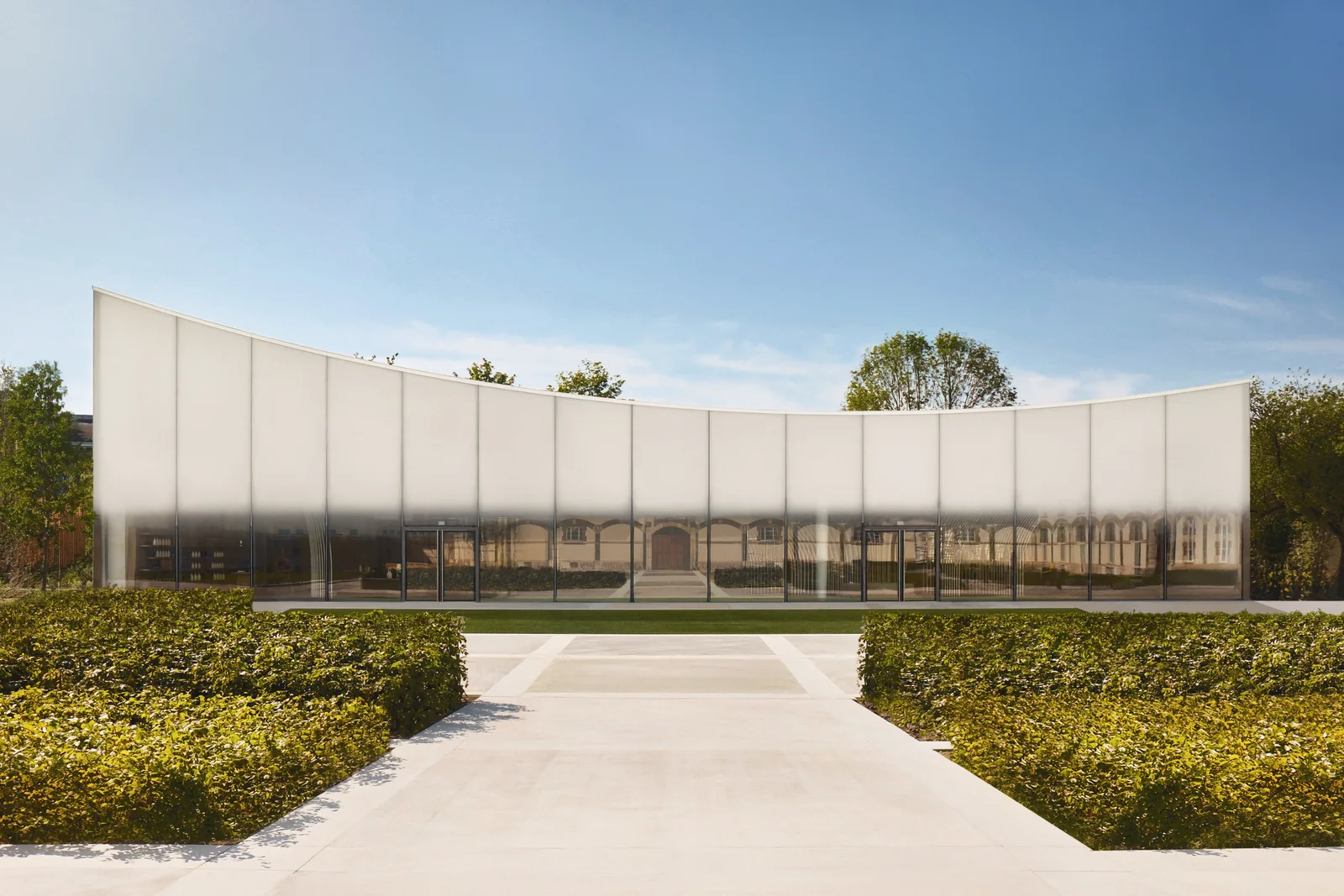 The façade of the Pavillon Nicolas at Ruinart, a long curved translucent wall reflecting the historic buildings behind it