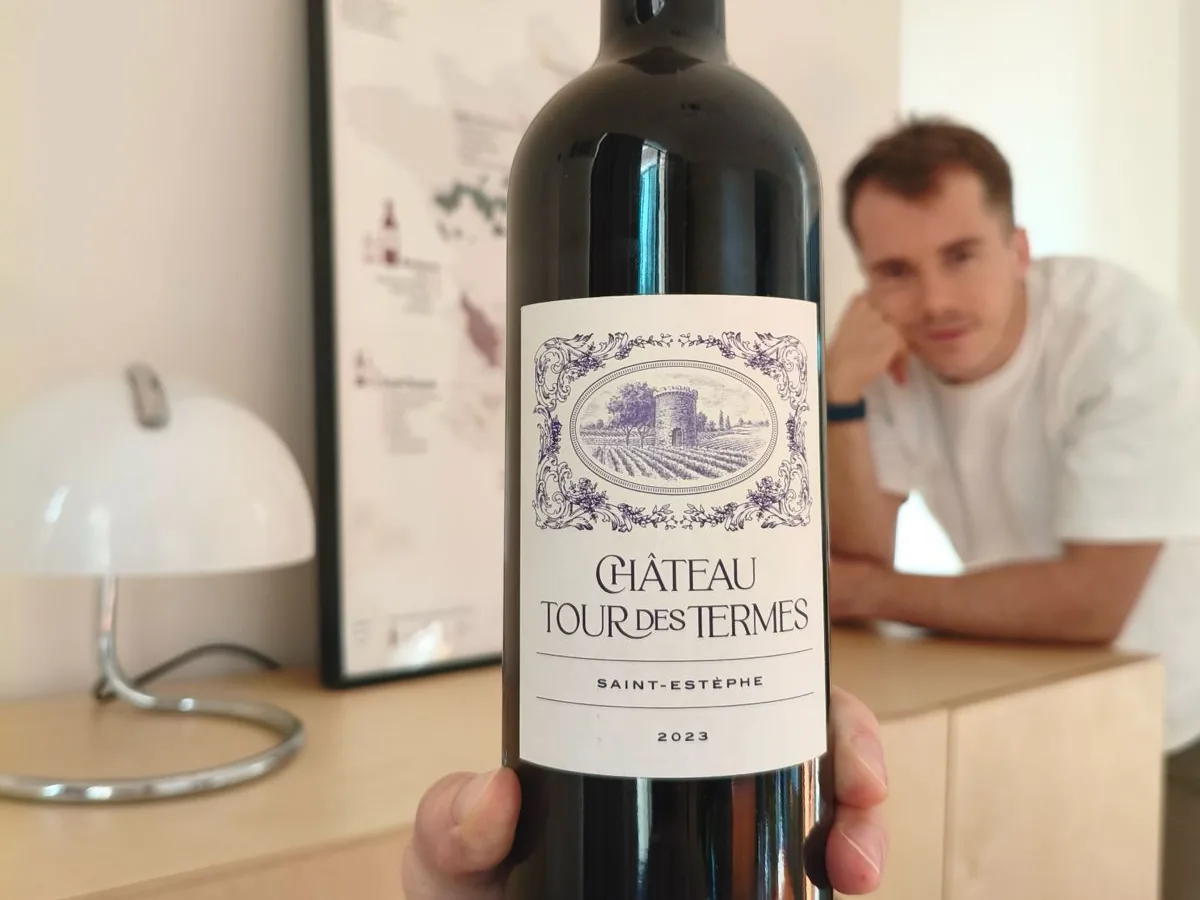 A bottle of Château Tour des Termes Saint-Estèphe 2023 held up close, its white label showing an engraved tower among vines in an oval frame