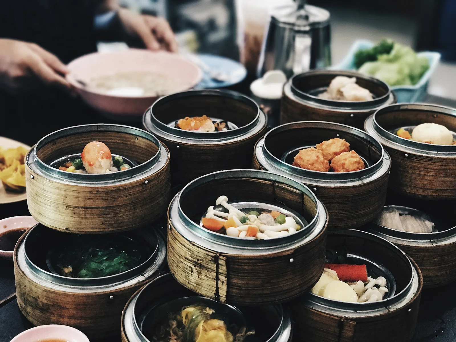 Bamboo steamer baskets of dim sum crowded on a Hong Kong breakfast table, with prawn dumplings, fish balls and mushrooms, a teapot behind